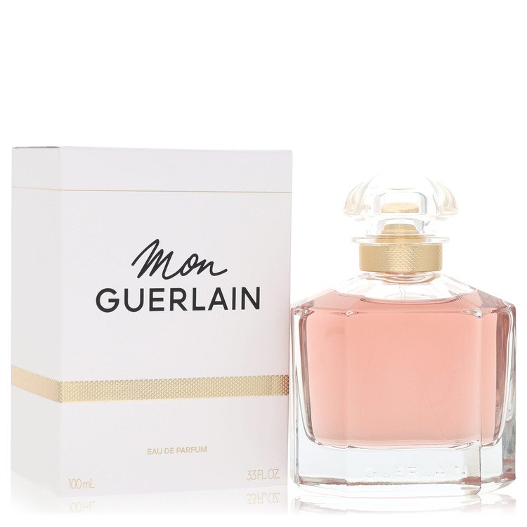 Guerlain Mon Guerlain Eau de Parfum bottle with pink liquid next to its white and gold packaging box on a white background.
