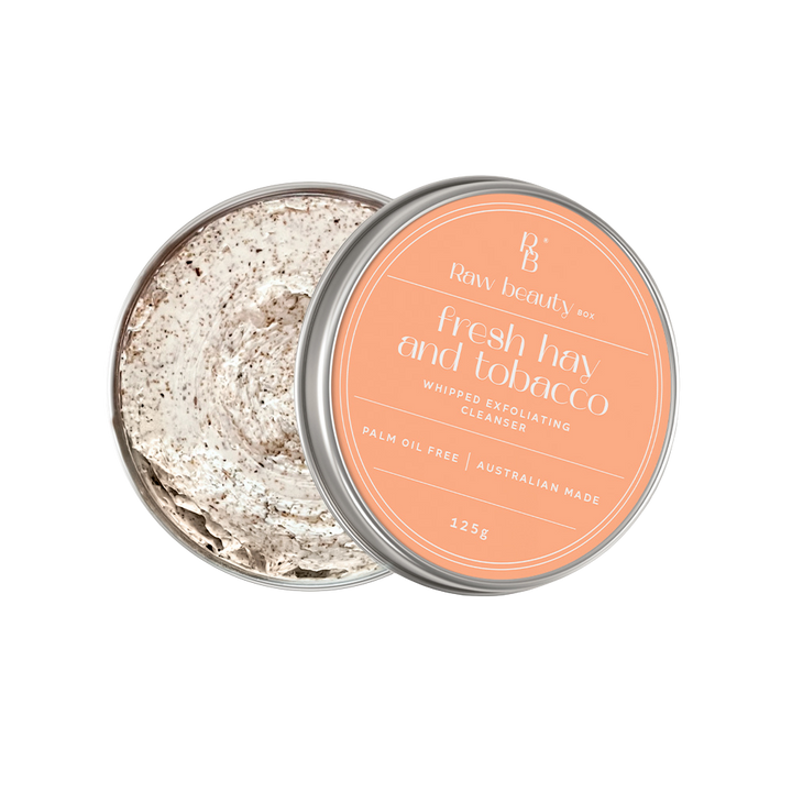 Open tin of 'Fresh hay and tobacco' whipped exfoliating cleanser with visible powder inside, on a white background.