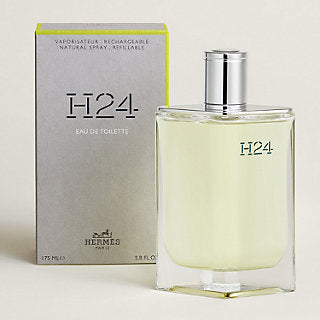 Hermès H24 Eau de Toilette perfume bottle with a silver cap next to its gray packaging box, on a light beige background.